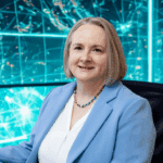 Alexandra Kärgel, Unternehmerin und Expertin für Nachfolge im Familienunternehmen, arbeitet an ihrem Schreibtisch mit digitalen KI-Technologien. Der Hintergrund zeigt ein modernes, holografisches Netzwerk – Symbol für Zukunft, Innovation und verantwortungsvollen KI-Einsatz.