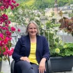 Alexandra Kärgel auf ihrem blühenden Balkon. Sie trägt ein gelbes Shirt mit einer blauen Shirtjacke