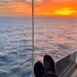 Selbstfürsorge als Nachfolgerin: Sonnenuntergang über dem Meer, vom Balkon eines Kreuzfahrtschiffs aus gesehen, mit hochgelegten Füßen von Alexandra Kärgel